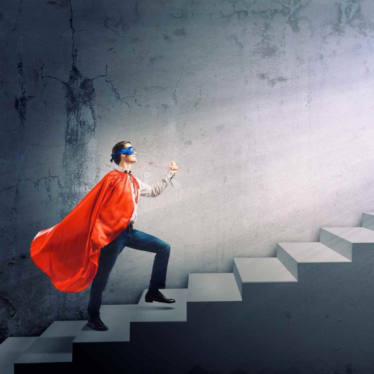 A man in a business suit wearing a superhero cape and mask climbing some stairs.